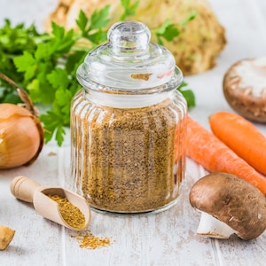 Un pot de bouillon en poudre entouré de légumes frais.