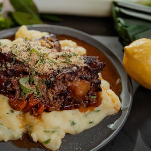 Un braisé de boeuf servi sur des pommes de terre écrasées et un citron entier posé sur la table, appuyé sur l'assiette.