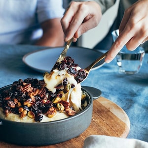 Une personne sert une portion de brie fondant aux pistaches, pacanes et canneberges.