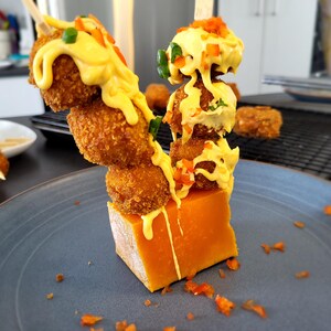 Deux brochettes de croquettes de poulet et sauce au fromage sont piquées sur un bloc de fromage.