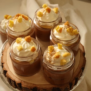 Des verrines remplies de mousse au chocolat et de génoise. Elles sont garnies avec de la crème fouettée et des petits cubes de génoise.