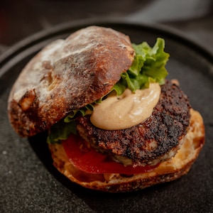 Un burger garni de laitue, d'une tranche de tomate, d'une boulette de viande et de sauce dans une assiette noire.