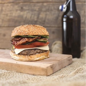 Un burger garni de fromage, de tomates, de laitue et de bacon posé sur une planche en bois.
