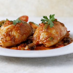 Deux calmars farcis nappés de sauce tomate, dans une assiette.