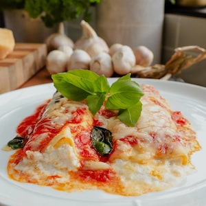 Deux cannellonis farcis, nappés de sauce tomate, gratinés et garnis de basilic frais.