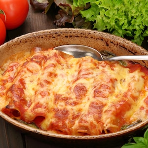 Dans un plat ovale, il y a des cannellonis farcis cuits dans de la sauce béchamel et de la sauce tomate.