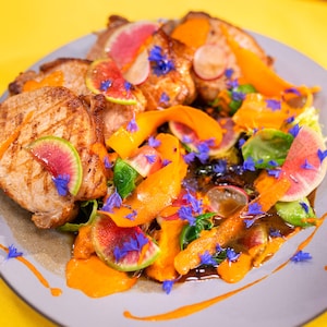 Des carrés de porc rôti disposés dans une assiette et garnis de légumes tranchés finement à la mandoline.