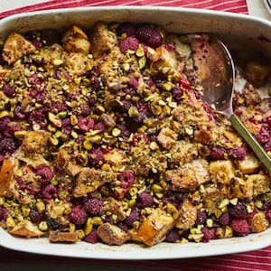 Un plat de pain doré aux framboises et aux pistaches avec une cuillère.