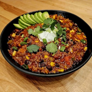 Un bol de chili au quinoa servi avec des tranches d'avocat, de la crème sure et des feuilles de coriandre.