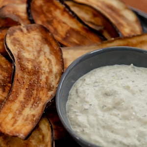 Des chips d'aubergines dans une assiette avec un bol rempli de tzatziki au labneh.