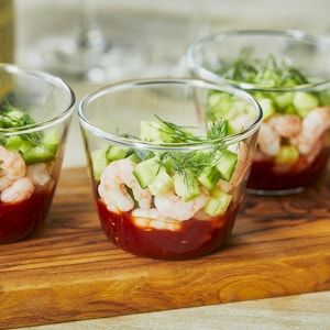 Quatre cocktails de crevettes nordiques sur une planche à découper en bois.