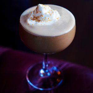Un cocktail brun dans une coupette avec de la mousse blanche.