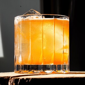 Un cocktail orangé avec de la glace sur une bûche du bois.