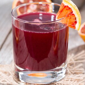 Un verre rempli d'un cocktail rouge foncé entouré d'oranges sanguines.
