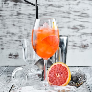 Un cocktail orange dans une coupe de vin, un demi-pamplemousse, un mélangeur à cocktail.
