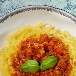 Courge spaghetti garnie de sauce sauce bolognaise végane et de feuilles de basilic.