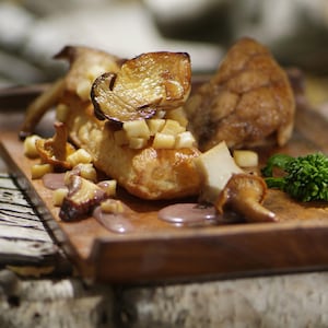 Ris de veau cuits décorés de champignons sauvages rôtis dans une assiette en bois.