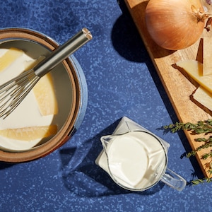 Crème croûte aux parmesan dans une casserole. Oignons, ail, fromage et romarin sur une planche.