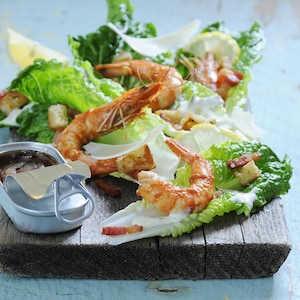 Des feuilles de laitue romaine avec crevettes entières et quartiers de citron sur une planche de bois.