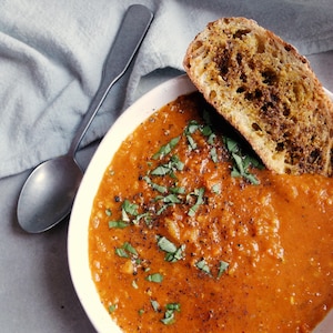 Vue en plongée sur un bol de soupe de lentilles avec un croûton trempant dans la soupe et une cuillère posée à côté du bol.