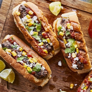 Quatre dogburgers à la mexicaine sur une planche de bois.