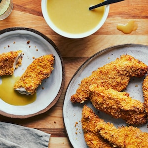 Deux assiettes de doigts de poulet panés sur un comptoir en bois, avec une salade et une sauce. 