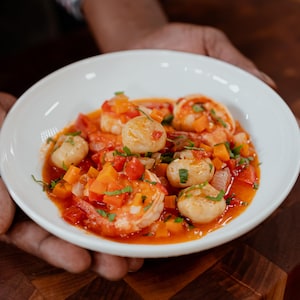 Des crevettes et des pétoncles recouverts de légumes et de sauce dans un bol.