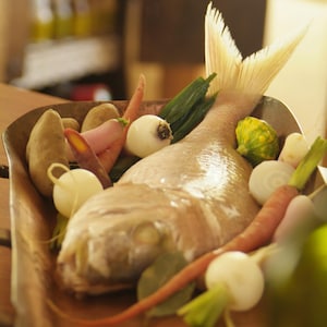 Un poisson entier dans un plat et entouré de légumes.