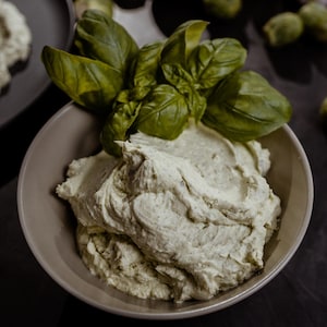 Un bol rempli d'émulsion de fromage de chèvre garnie de feuilles de basilic.