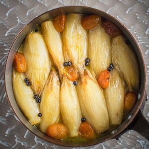 Une casserole d'endives confites avec des kumquuats et des baies de genièvre.