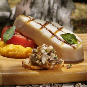 Un morceau de poisson blanc grillé, des champignons, une tomate grillée et de la purée de patate douce sur une planche de bois.