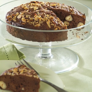 Un gâteau au chocolat garni de noix sur un présentoir à gâteau en vitre.