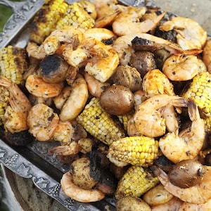 Un mélange de crevettes de morceaux de saucisses, de morceaux d'épis de maïs et de patates grelots grillés sur une plaque de cuisson à l'ancienne.