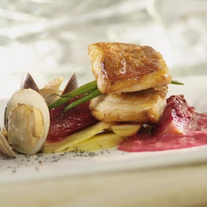 Un filet de sébaste dans une assiette accompagné de légumes et d'une purée de figues rose.