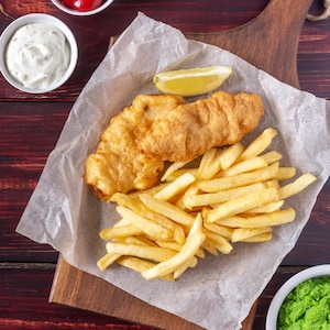 Un fish and chips servi sur une planche avec trois sauces différentes.
