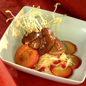 La recette de foies de canard avec des prunes sauvages reposant dans un petit plat blanc. 