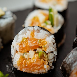 Des futomakis au saumon épicé sur un plateau à sushi.