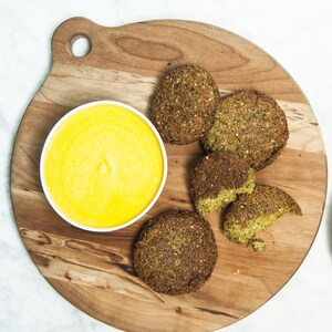 Des galettes de falafel servies sur une planche de bois, accompagnées d'une sauce au piment jaune et d'une gamme d'épices péruviennes.