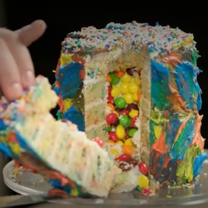 Un gâteau tartiné de glaçage multicolore et qui est farci de bonbons.