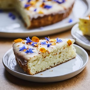 Un morceau de gâteau au citron avec des pétales de fleurs oranges et mauves sur le dessus. 