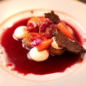 Un dessert composé de morceaux de gâteau au chocolat, de fraises, de framboises et meringues nappés d'un coulis au vin rouge.