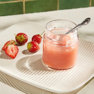 Dans une assiette, on retrouve des fraises ainsi qu'un pot qui contient du gel de fraises.