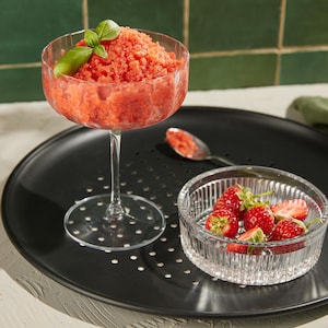 Une coupe remplie de granité aux fraises garnie de feuilles de basilic.