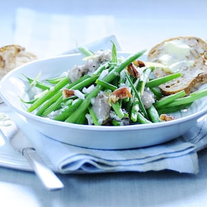 Un bol rempli de salade d'haricots verts, d'huîtres et de pacanes avec une tranche de pain beurrée. 