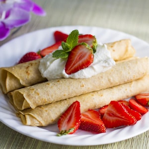 Des crêpes roulées garnies de crème fouettée et de morceaux de fraises.