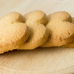 Quatre biscuits sablés en forme de coeur disposés sur une planche en bois.