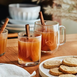 Sur une table est déposé trois verres contenant le jus de pomme chaud et une assiette de biscuits.