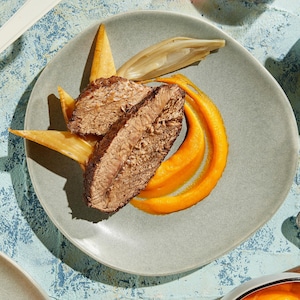Macreuse de boeuf dans une assiette sur une purée de carottes accompagnée de panais et échalotes rôtis.