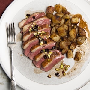 Un magret de canard tranché, servi avec des pommes de terre confites.