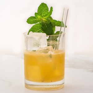 Un cocktail avec une paille en verre et des feuilles de menthe prêt à être dégusté.